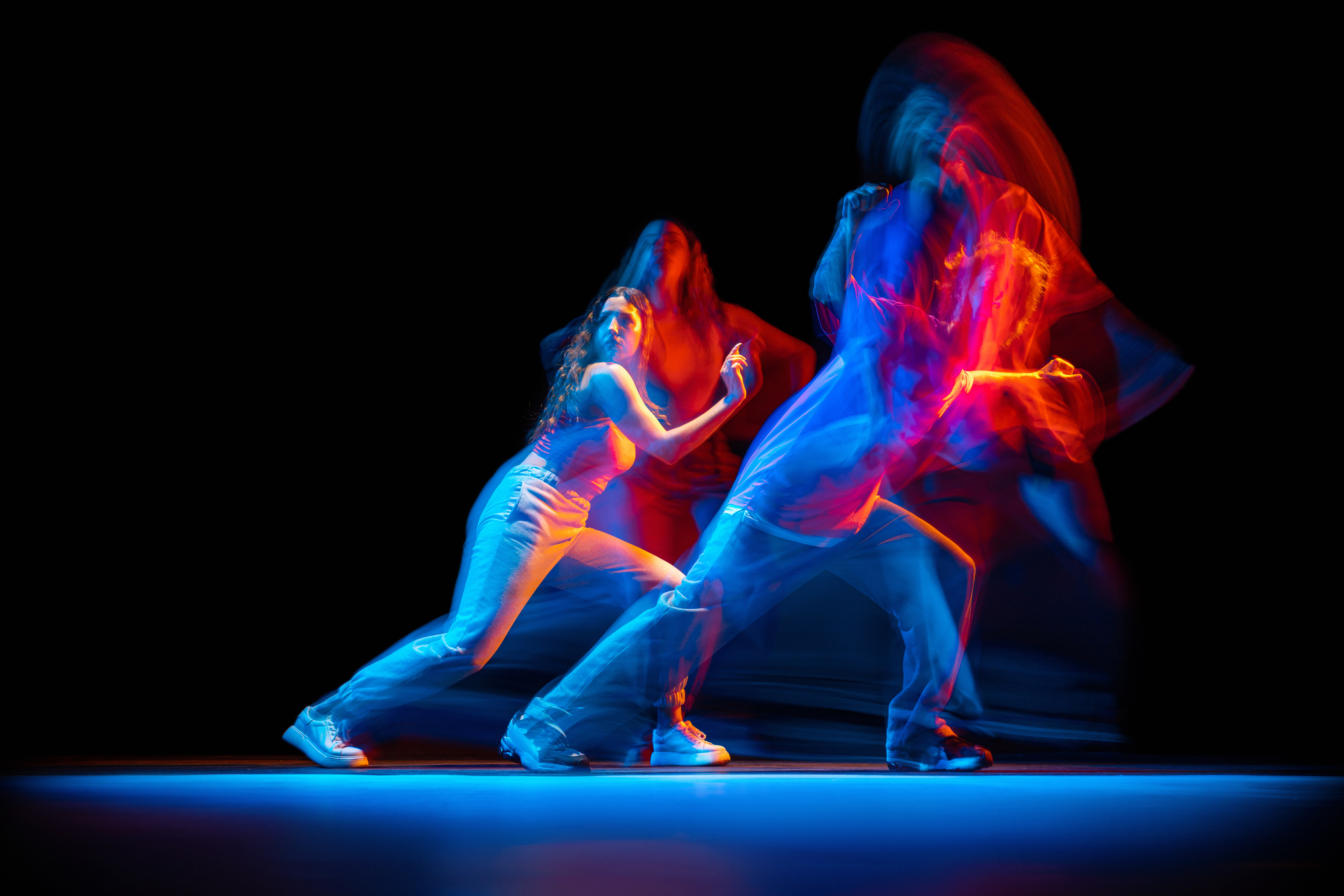 Dynamic portrait of young man and woman dancing hip-hop isolated over black background with mixed lights effect